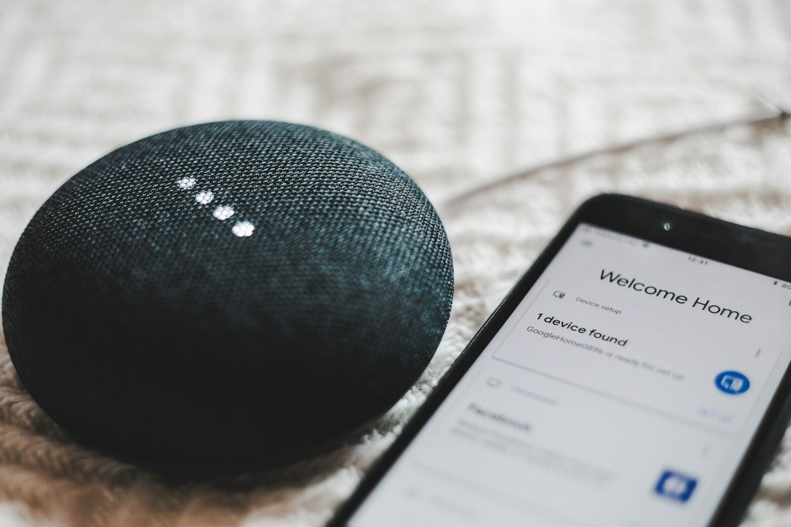 Charcoal smart speaker with glowing lights next to a smartphone, illustrating AI voice assistants