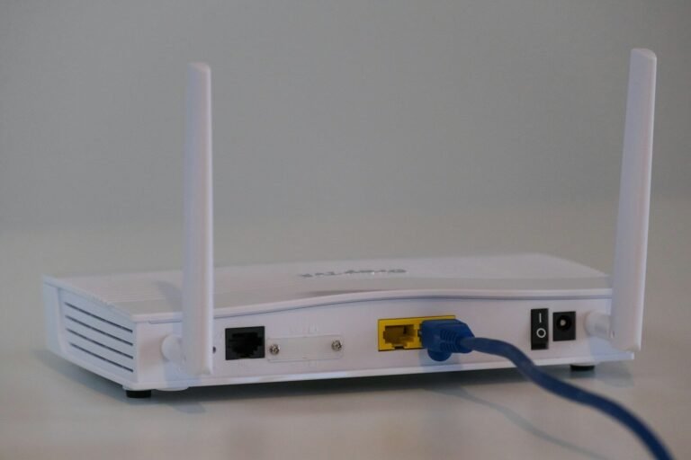 White Wi-Fi router with cables connected on a white table, illustrating a home Wi-Fi network setup guide