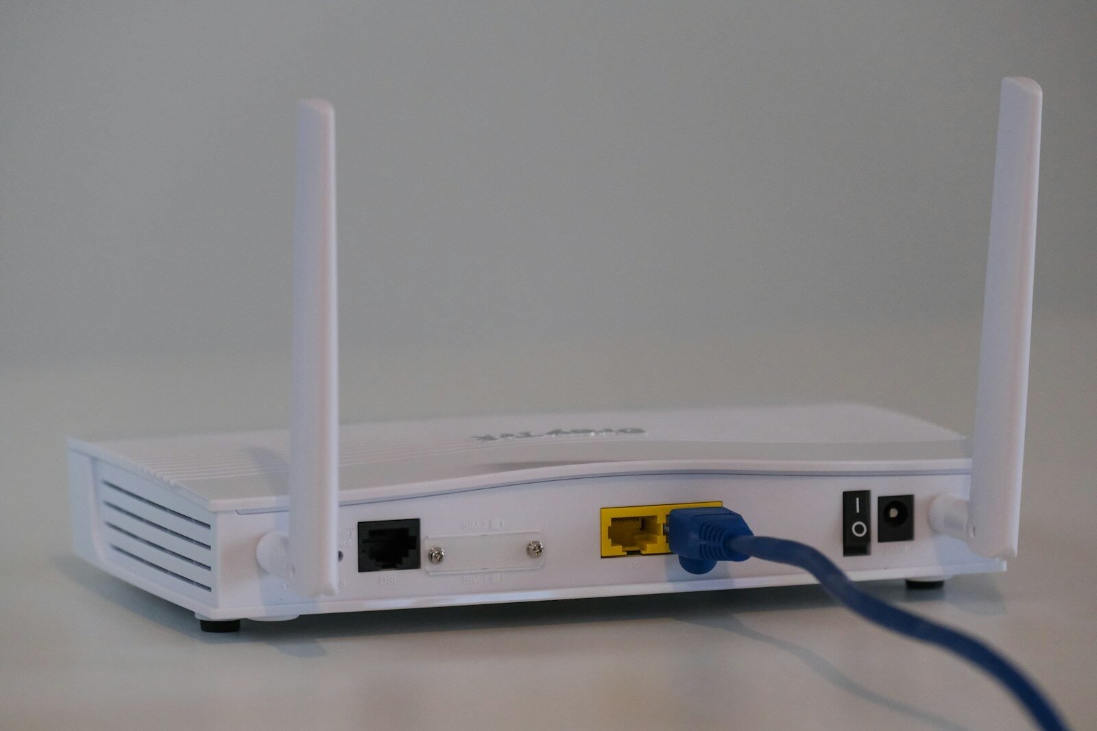 White Wi-Fi router with cables connected on a white table, illustrating a home Wi-Fi network setup guide
